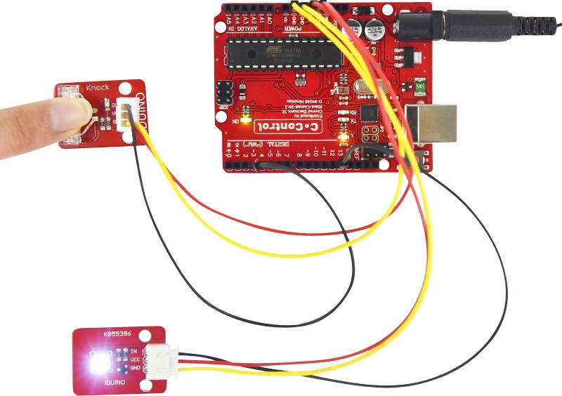 'Red open-source circuit board connected with cables. A blue LED light and a sensor are connected to the circuit board.'