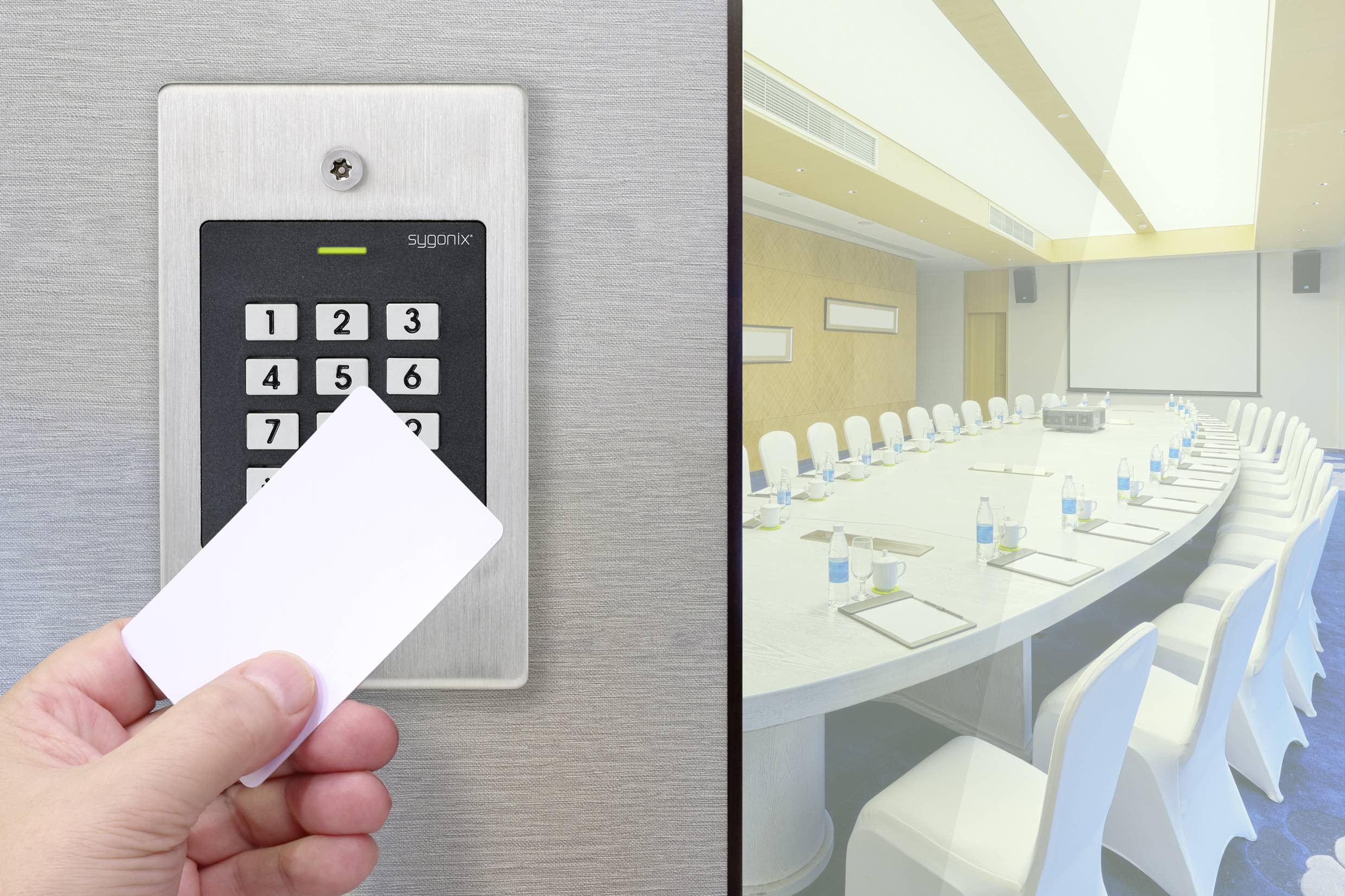 A hand holds an access card in front of a digital door lock. In the background, an empty conference room with a large table and chairs can be seen.