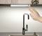 A hand moves over a modern kitchen tap, potentially for touchless activation of the water.