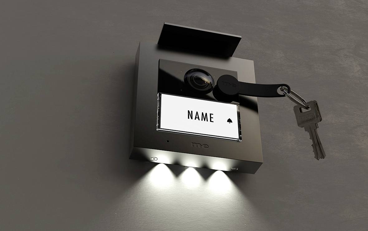 A modern video entry phone system with camera and nameplate. A key is inserted sideways in the lock.