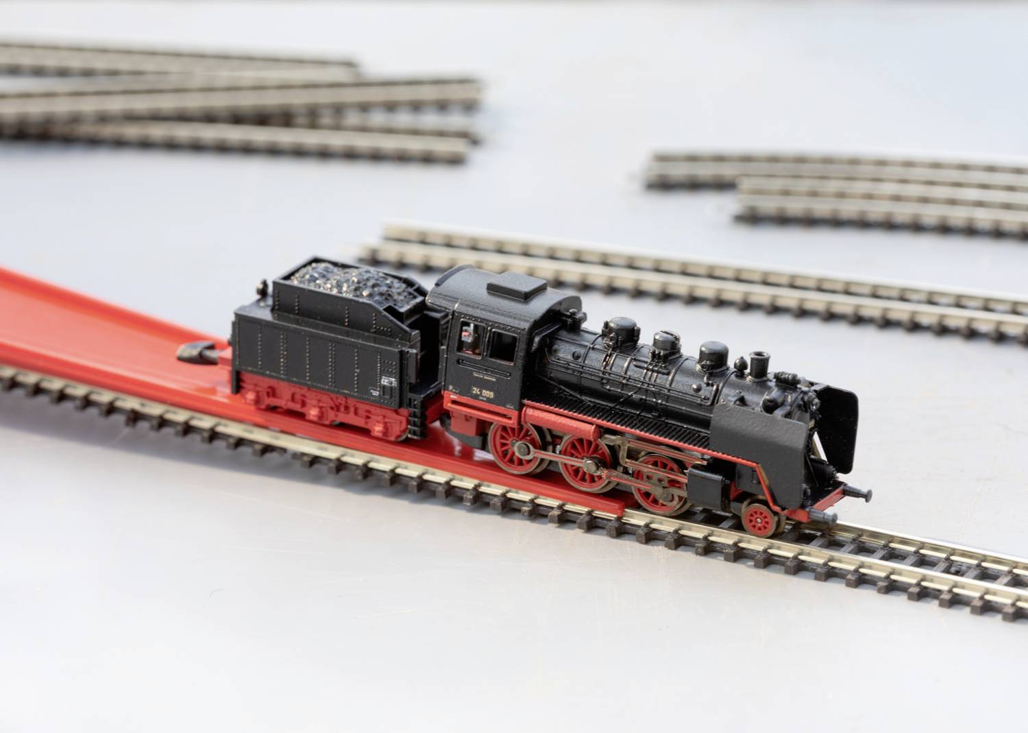 A black model locomotive with a red chassis stands on a railway track. Additional tracks can be seen in the background.