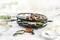 Raclette grill with various foods such as meat, vegetables and egg, surrounded by bowls of bread, salad and dip.