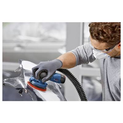 A person wearing safety goggles and a mask uses a power sander on a metallic surface, ensuring a smooth finish in a workshop setting.