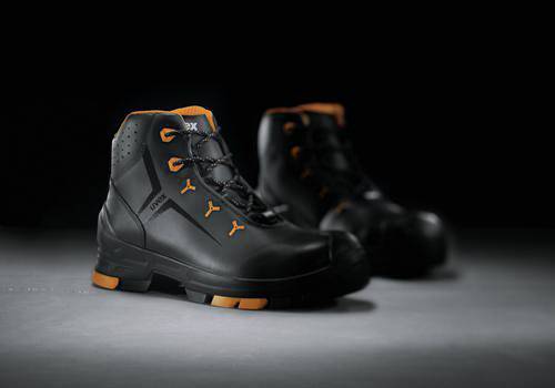 Black safety boots with orange accents, positioned on a grey surface, slightly in the background's shadow.