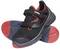 Black safety shoes with red sole and velcro fastening. Brand name on the fastener. Shoes stacked on top of each other.