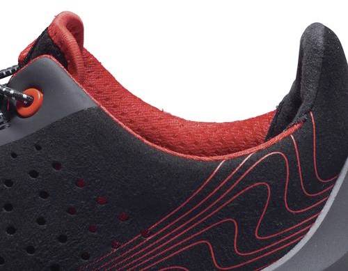 Black sports shoe with red accents, side close-up view. Distinctly visible, curved design with red shoelace eyelets.