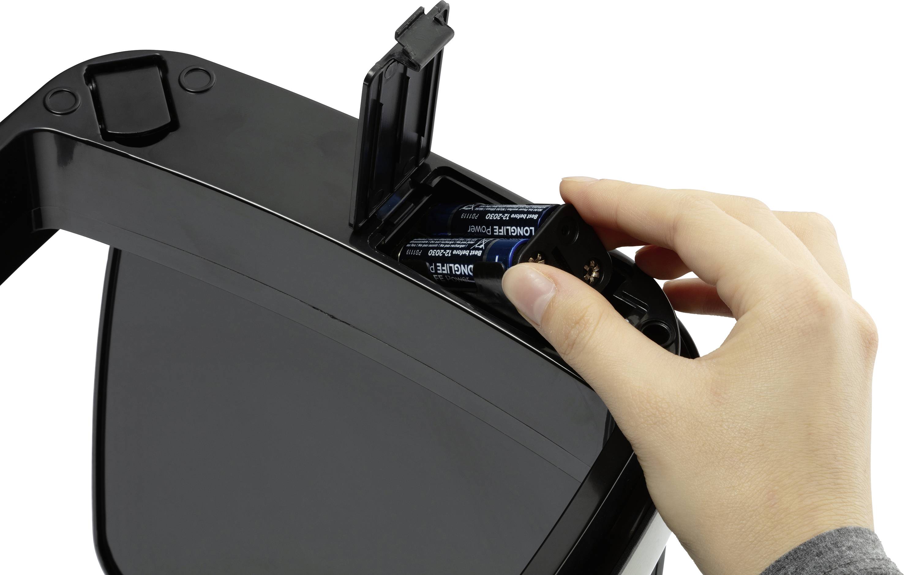 A person is inserting batteries into an electronic device with a battery compartment.