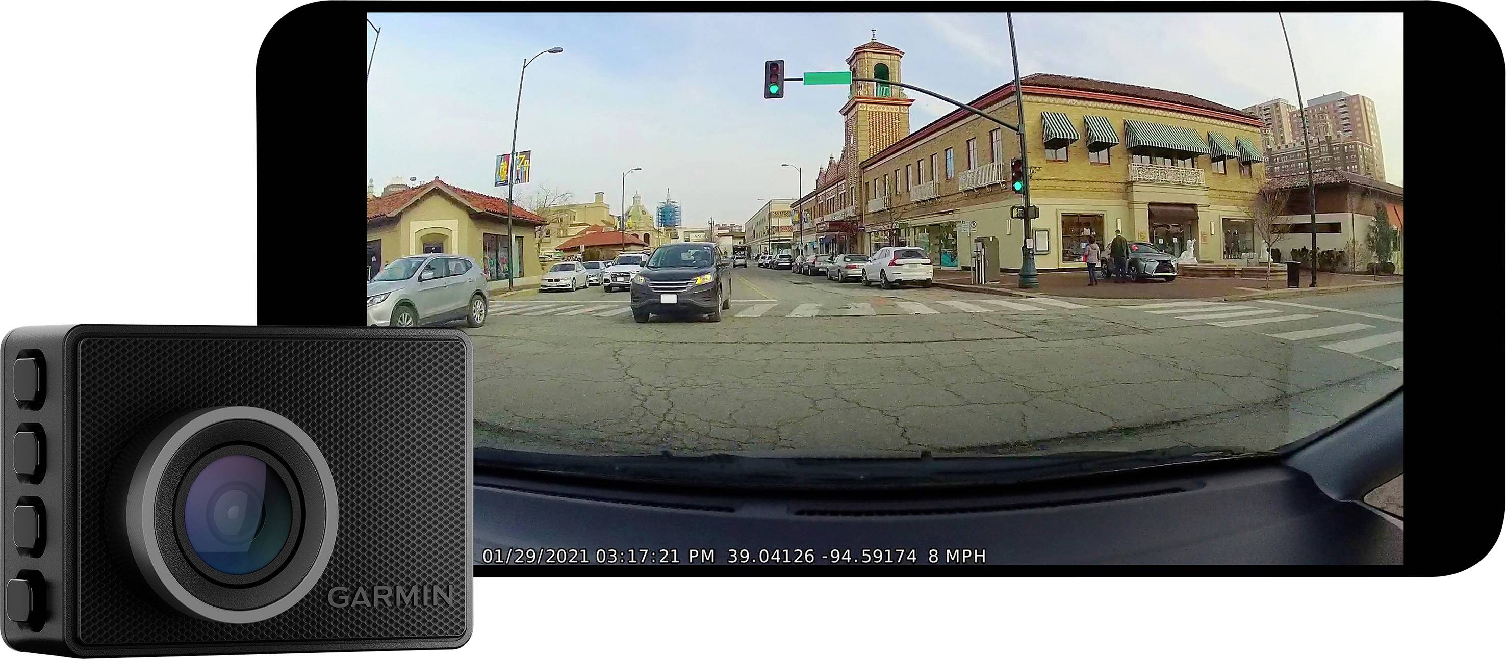 Image of a bustling street section with cars and shops, captured by a dashboard camera. A car is approaching a traffic light.