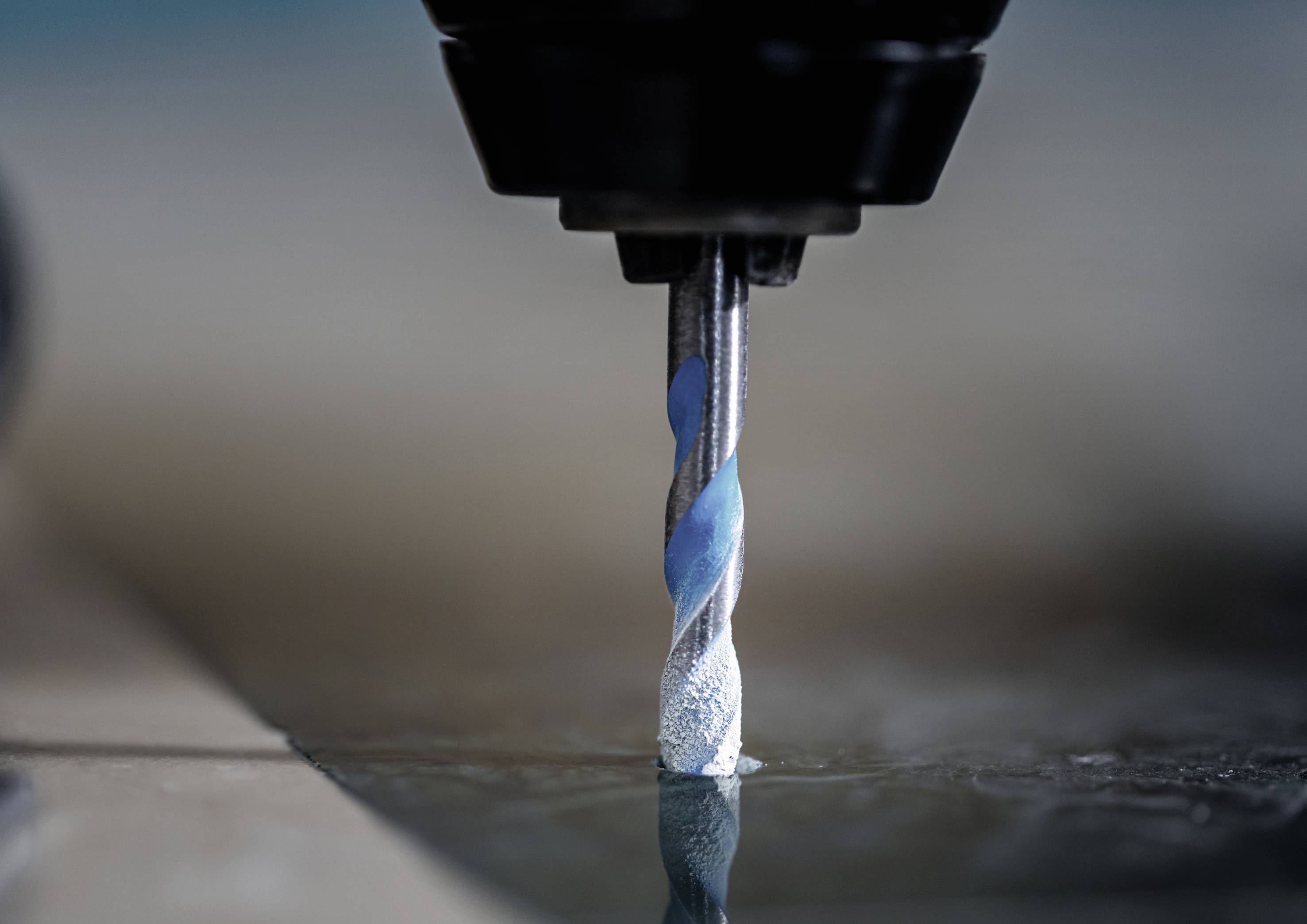 'Close-up of a drill bit drilling into a smooth surface, with metal shavings at the drilling point.'