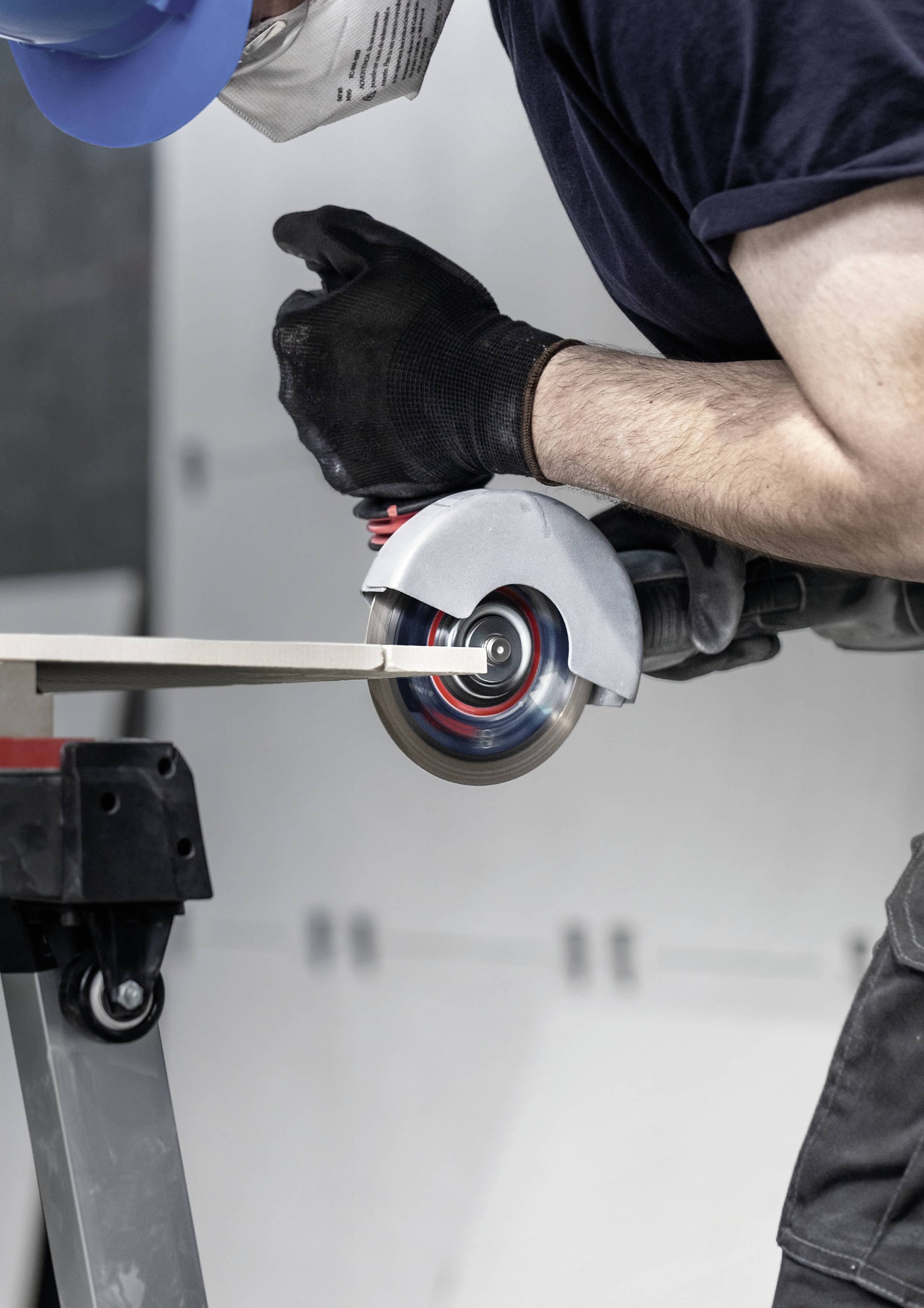 A person is working with a grinding machine on a metal piece, wearing a safety helmet and gloves in a workshop environment.