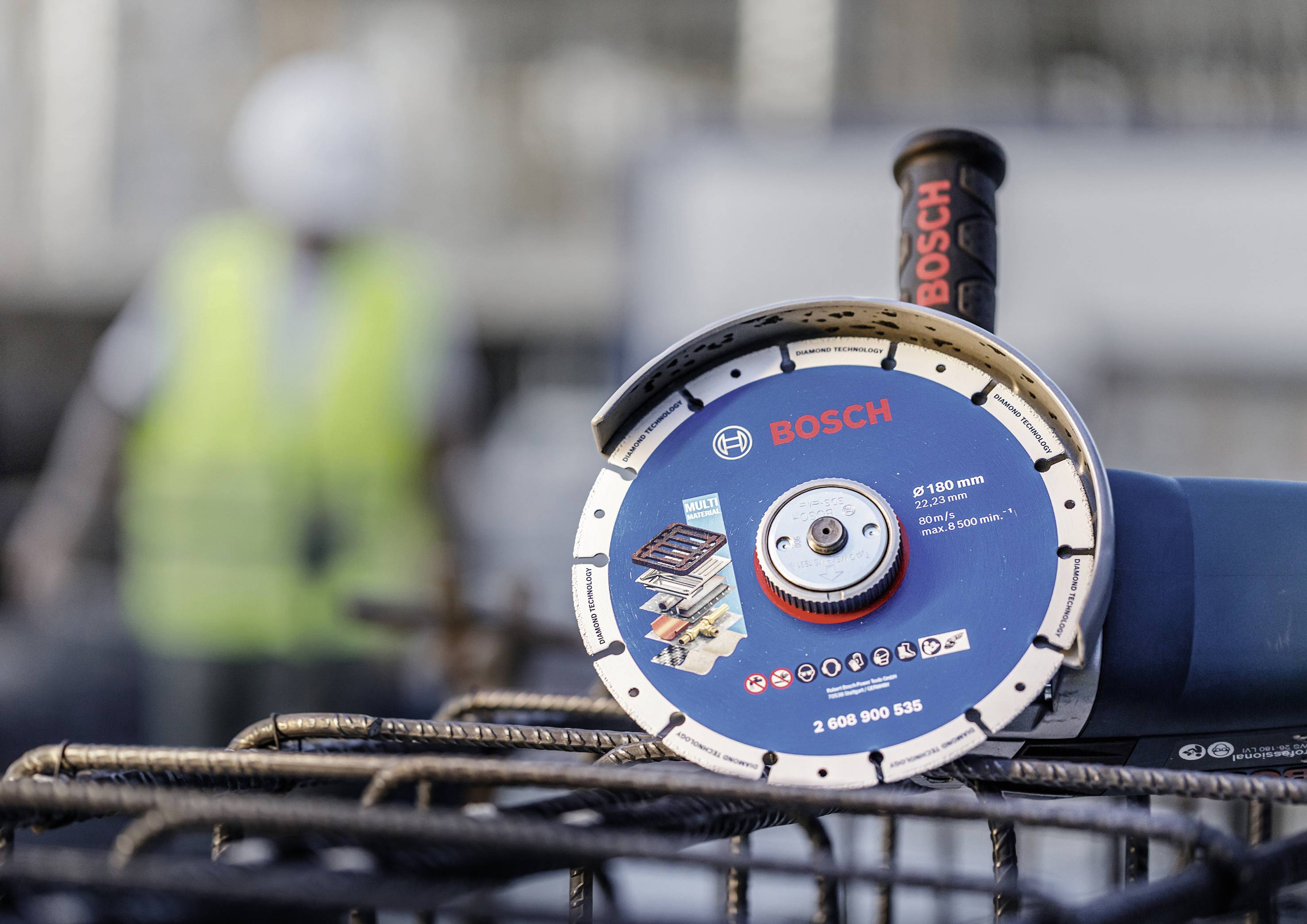 A Bosch angle grinder disc is in the foreground. In the background, a person in work attire is blurrily visible.