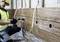 A worker in protective clothing is drilling a hole in a wooden board on a wall. Cables are hanging loosely down.