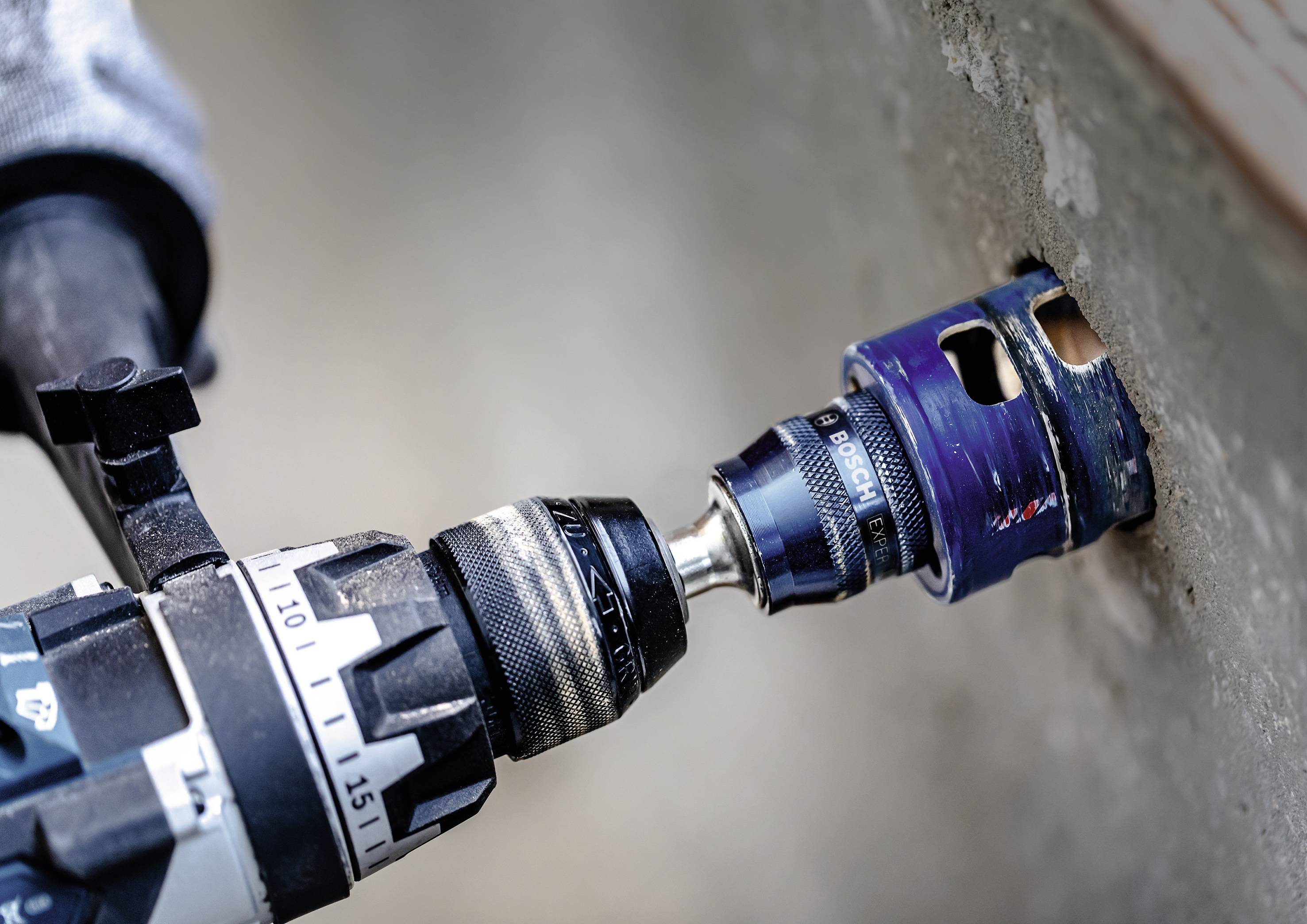A drill with a hole saw attachment is drilling a hole in a concrete wall.
