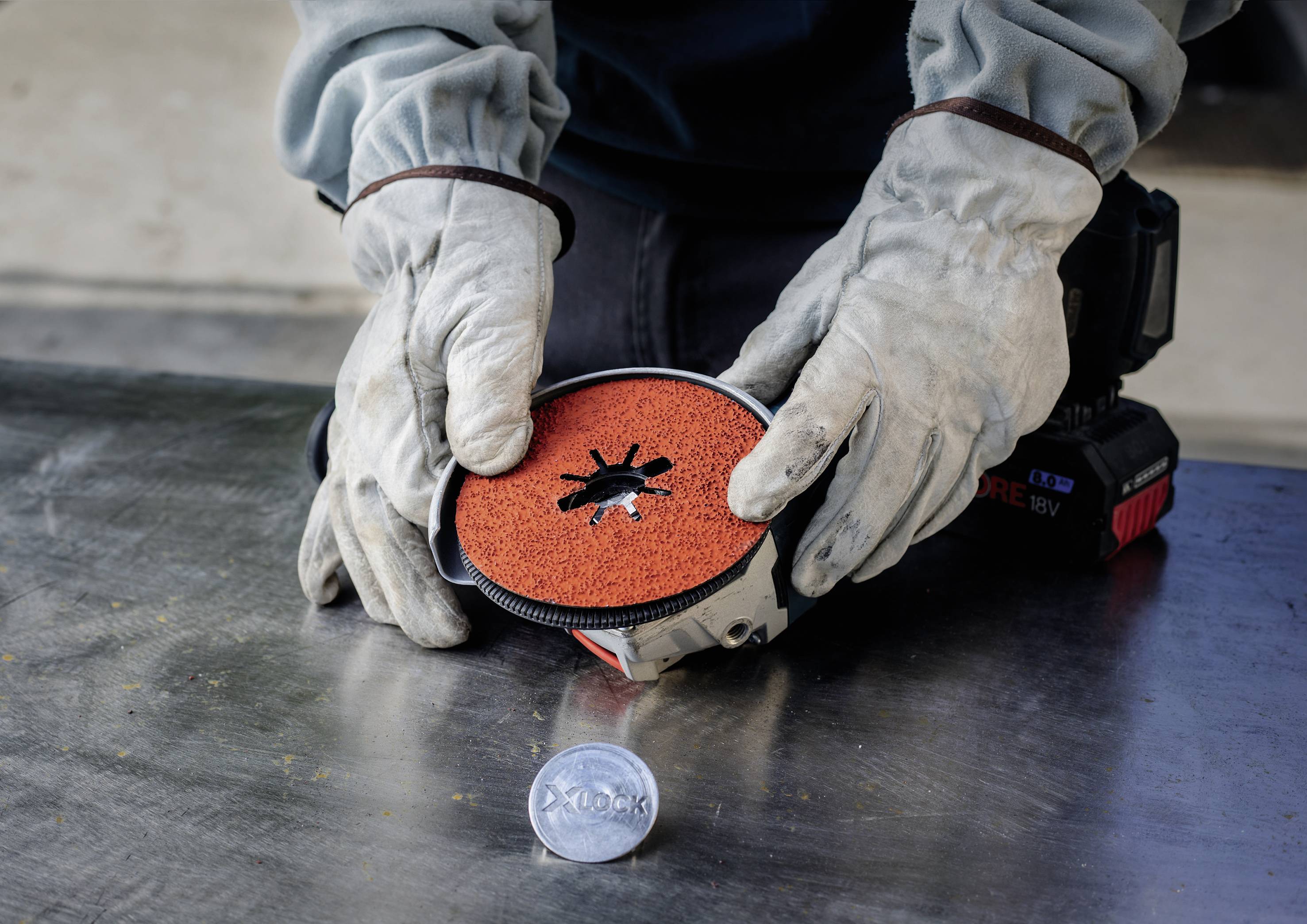 A person wearing gloves holding a grinding wheel on a table, with a round, metallic object beside it.