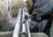 A worker in protective clothing is using an electric saw to cut a pipe on a construction site. Earth and pipes surround him.