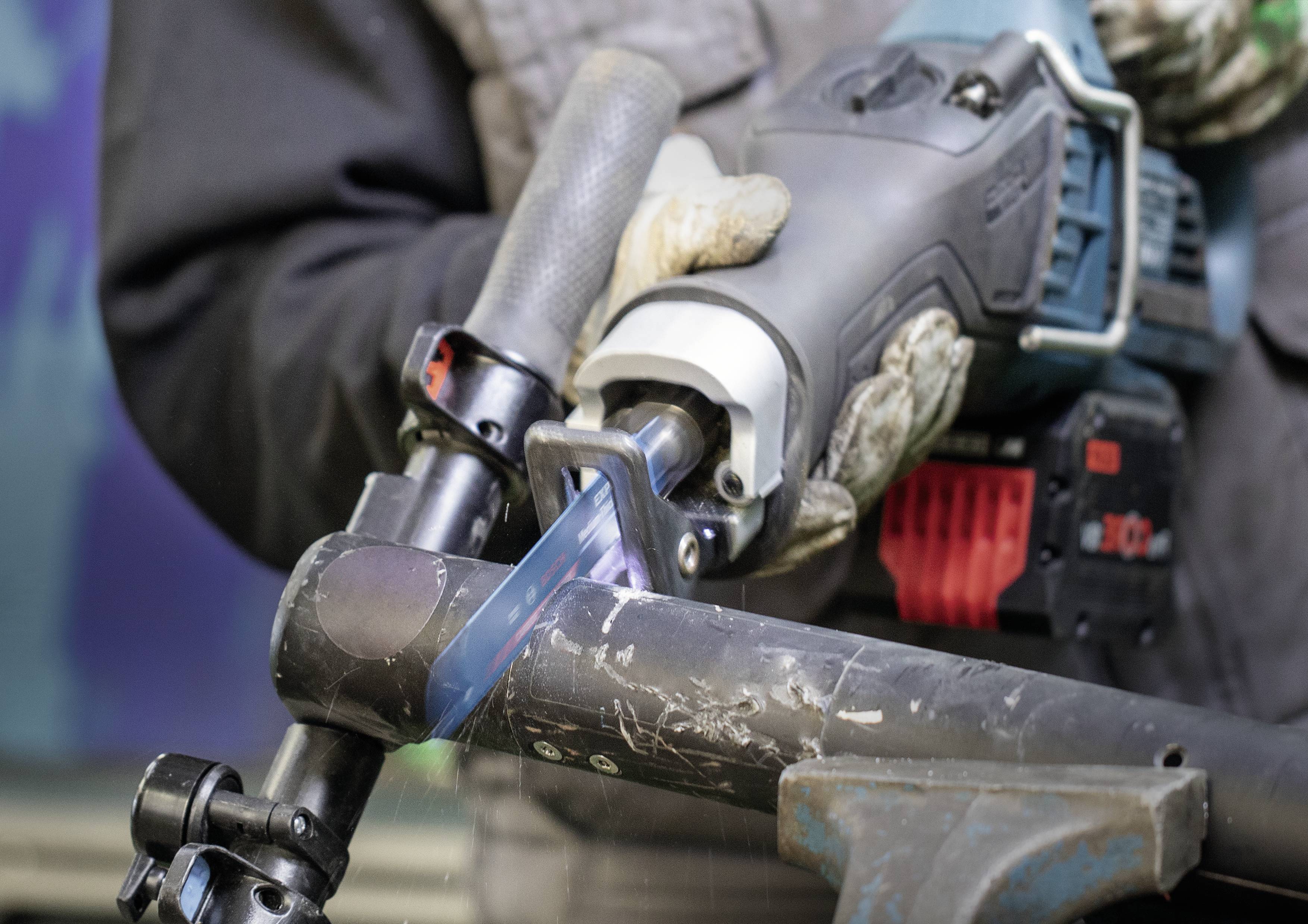 A person is cutting a metal pipe with an electric saw. The saw is generating sparks, indicating active machining.