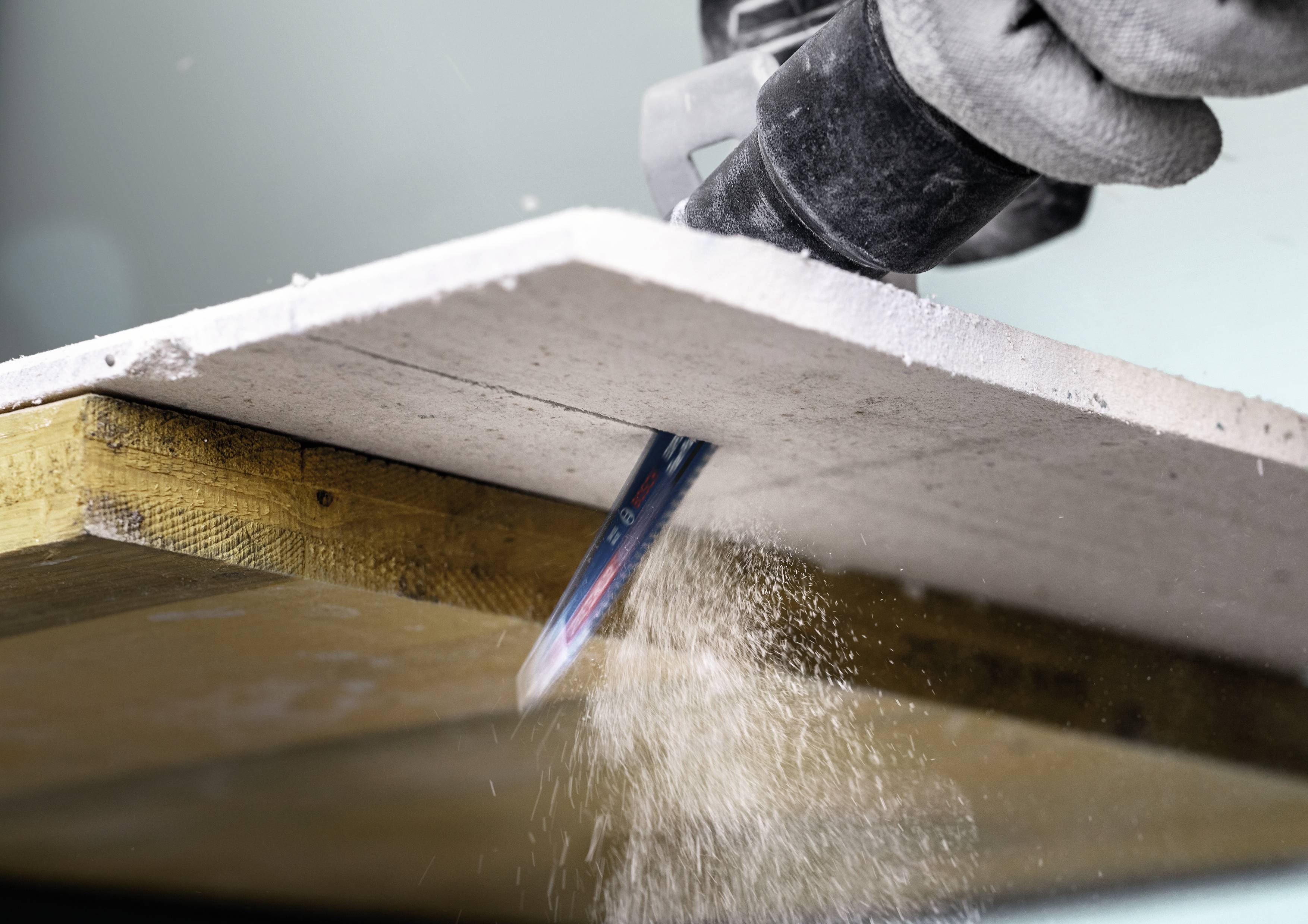 A person is cutting through a white plate with a machine, with dust flying from the cutting interface.