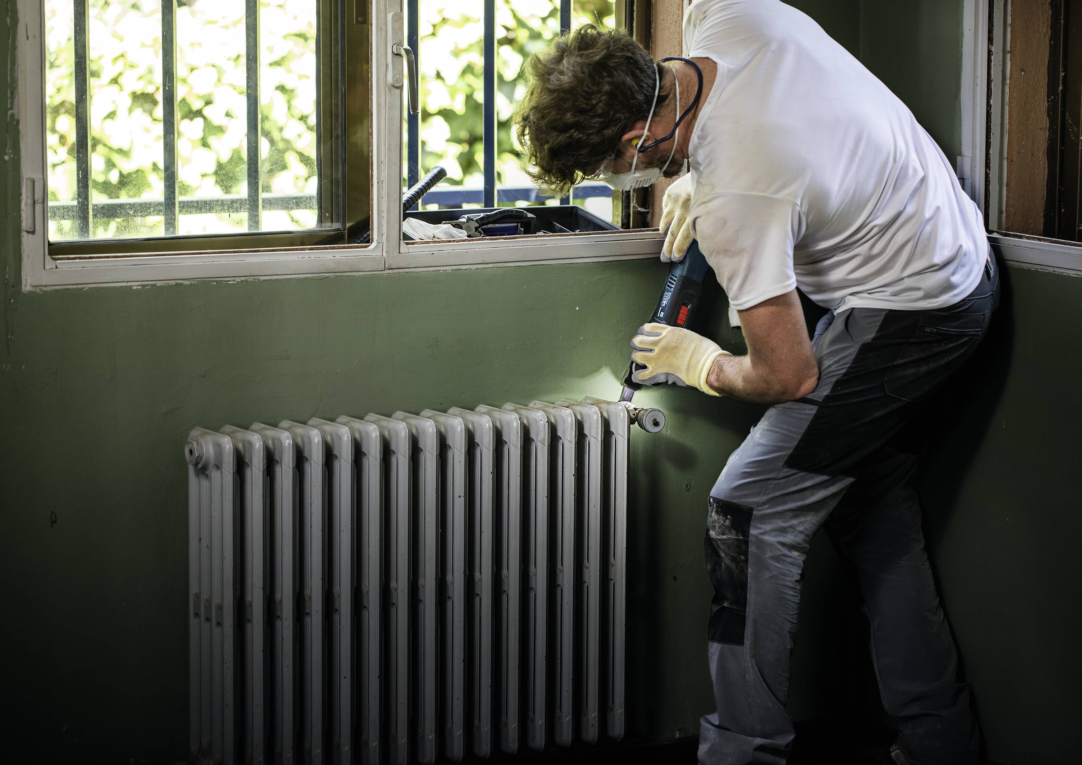 A person is working manually on a radiator in a room. They are wearing safety glasses and gloves, focusing intently on the repair.