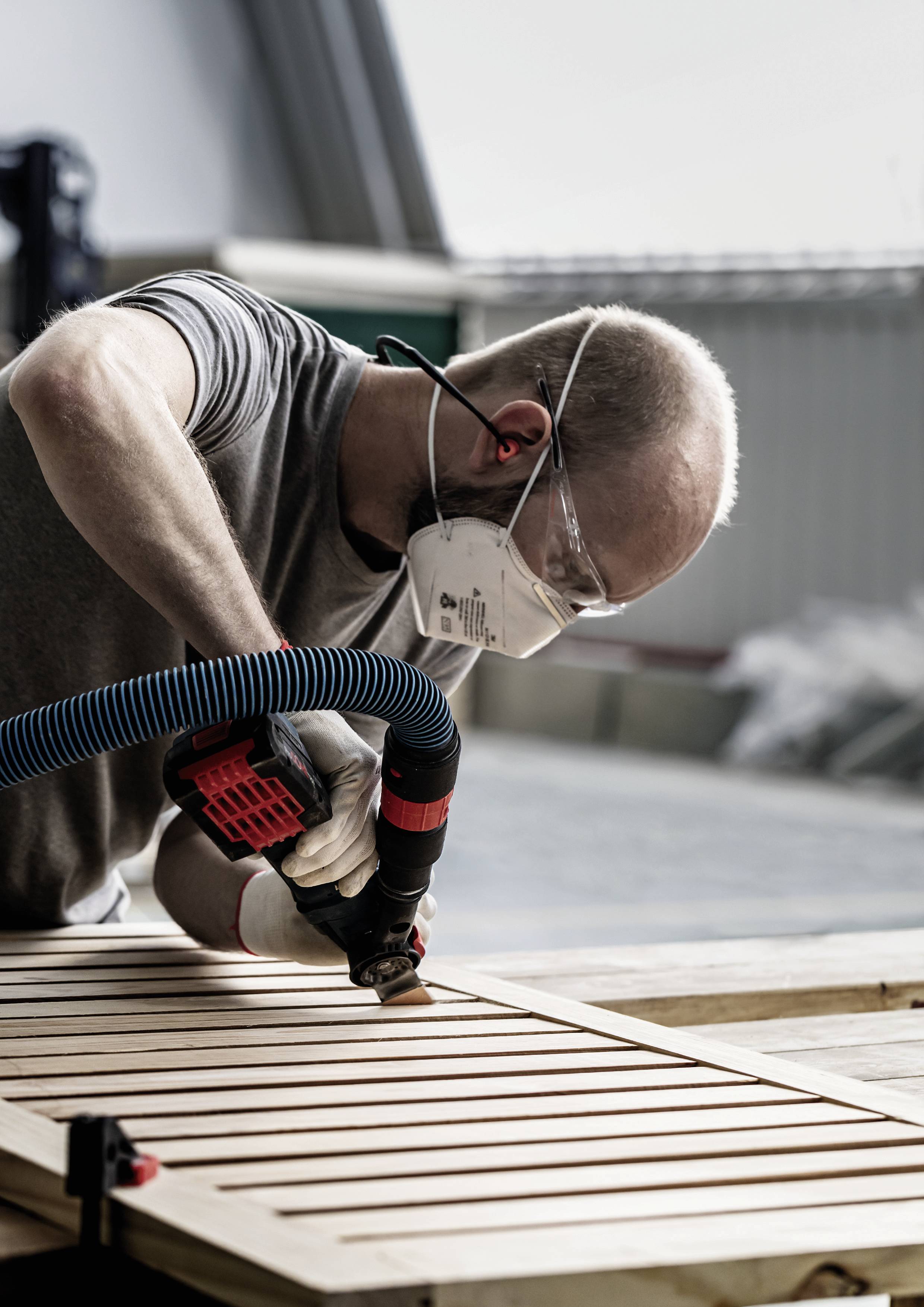 A man is working with a grinding machine on a wooden board in a workshop, wearing a protective mask and safety glasses, carefully and focused.