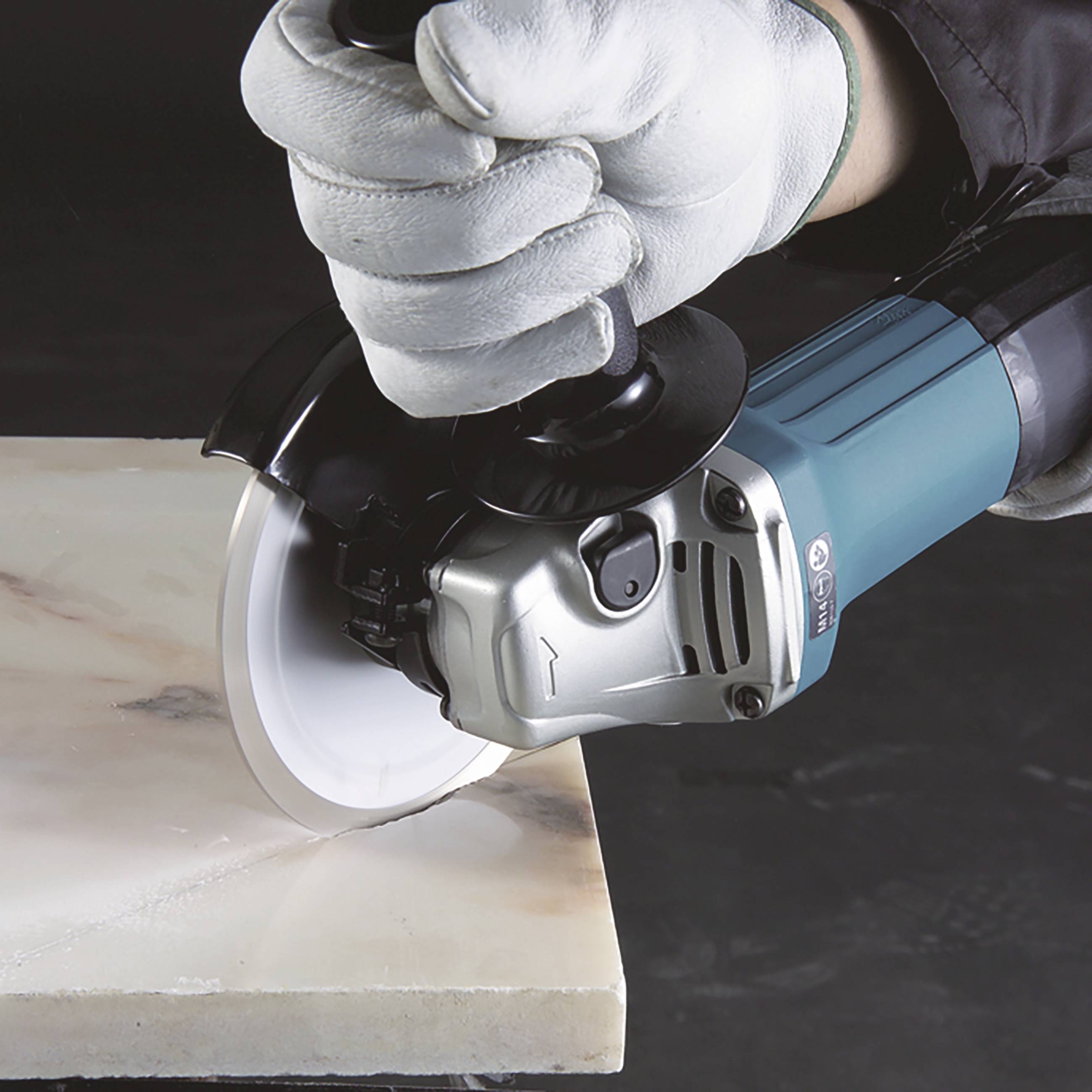 A worker wearing white gloves is cutting a marble slab with an angle grinder.