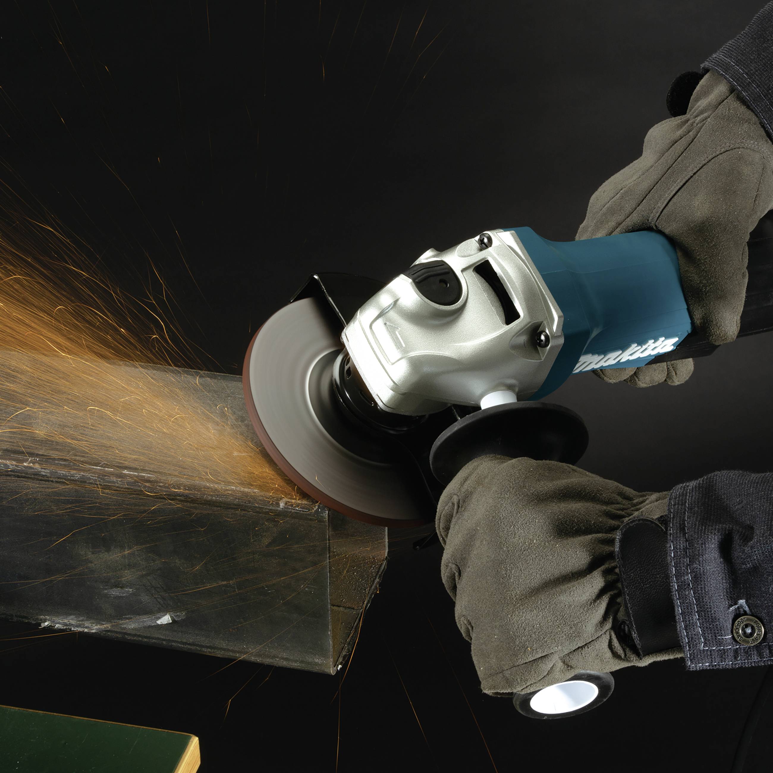 A person is grinding metal with an angle grinder. Sparks are flying from the cutting area. Wearing work gloves for safety.