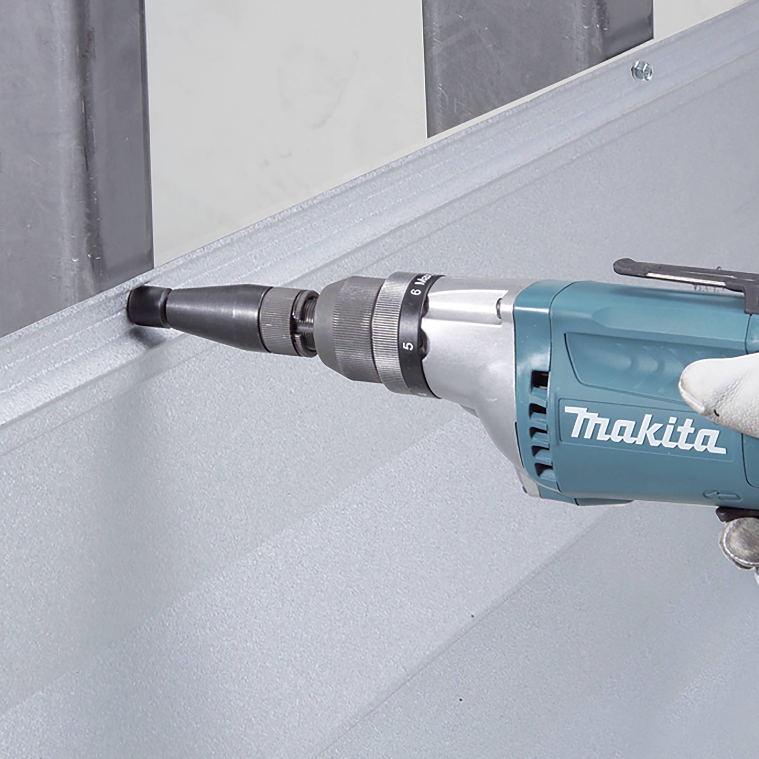 A person is using a cordless drill to screw a screw into a metal plate. The drill is blue and is a Makita brand.