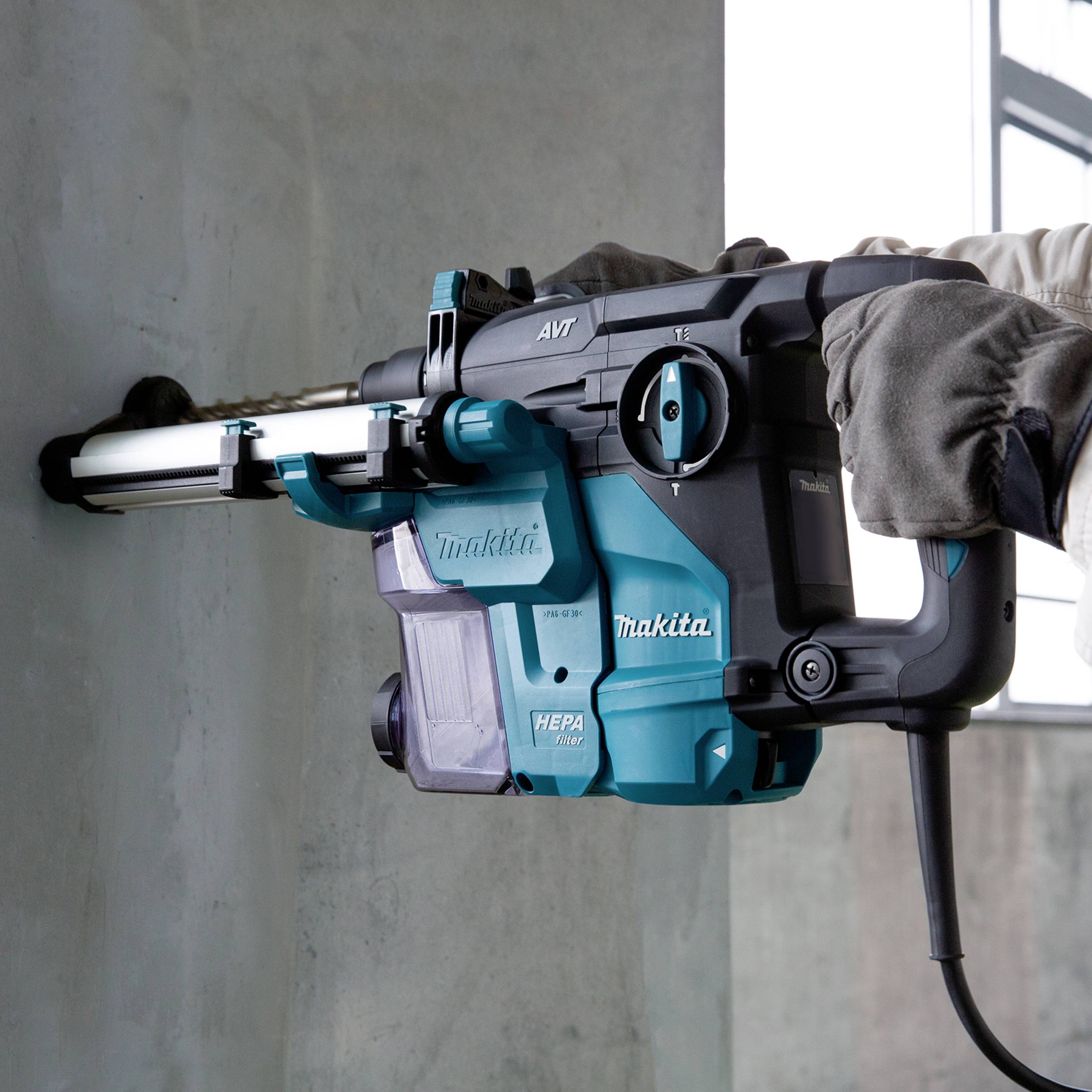 A tradesman is drilling a hole in a concrete wall using a blue drill hammer that vacuums dust through an attached hose.