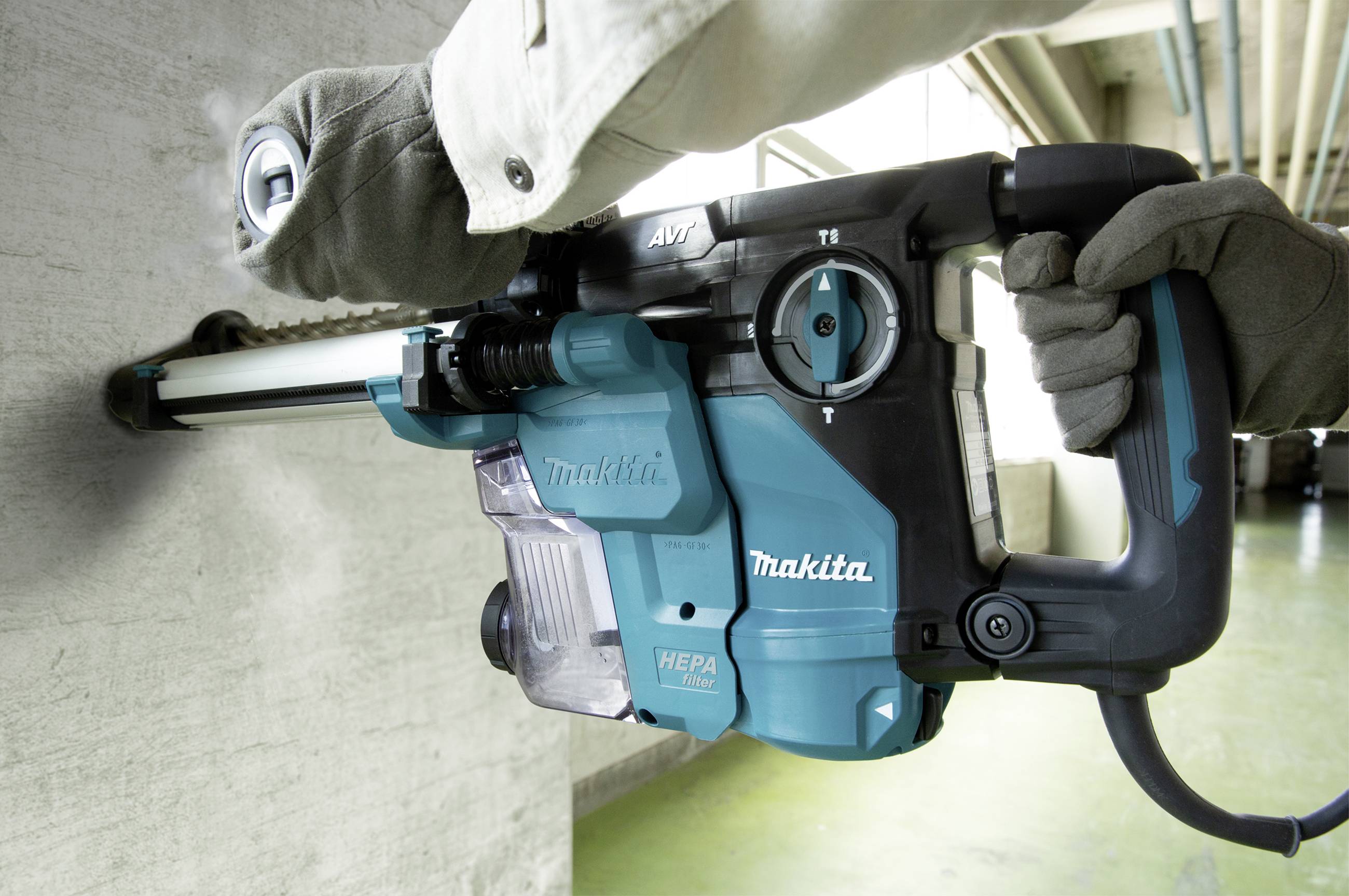 A person is drilling into a concrete wall using a blue hammer drill with a HEPA filter.