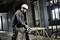 A construction worker wearing a hard hat is cutting wood with a circular saw in an unfinished building room. Construction site in the background.