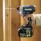 A person is drilling a hole in a wooden board using a blue Makita cordless drill driver.