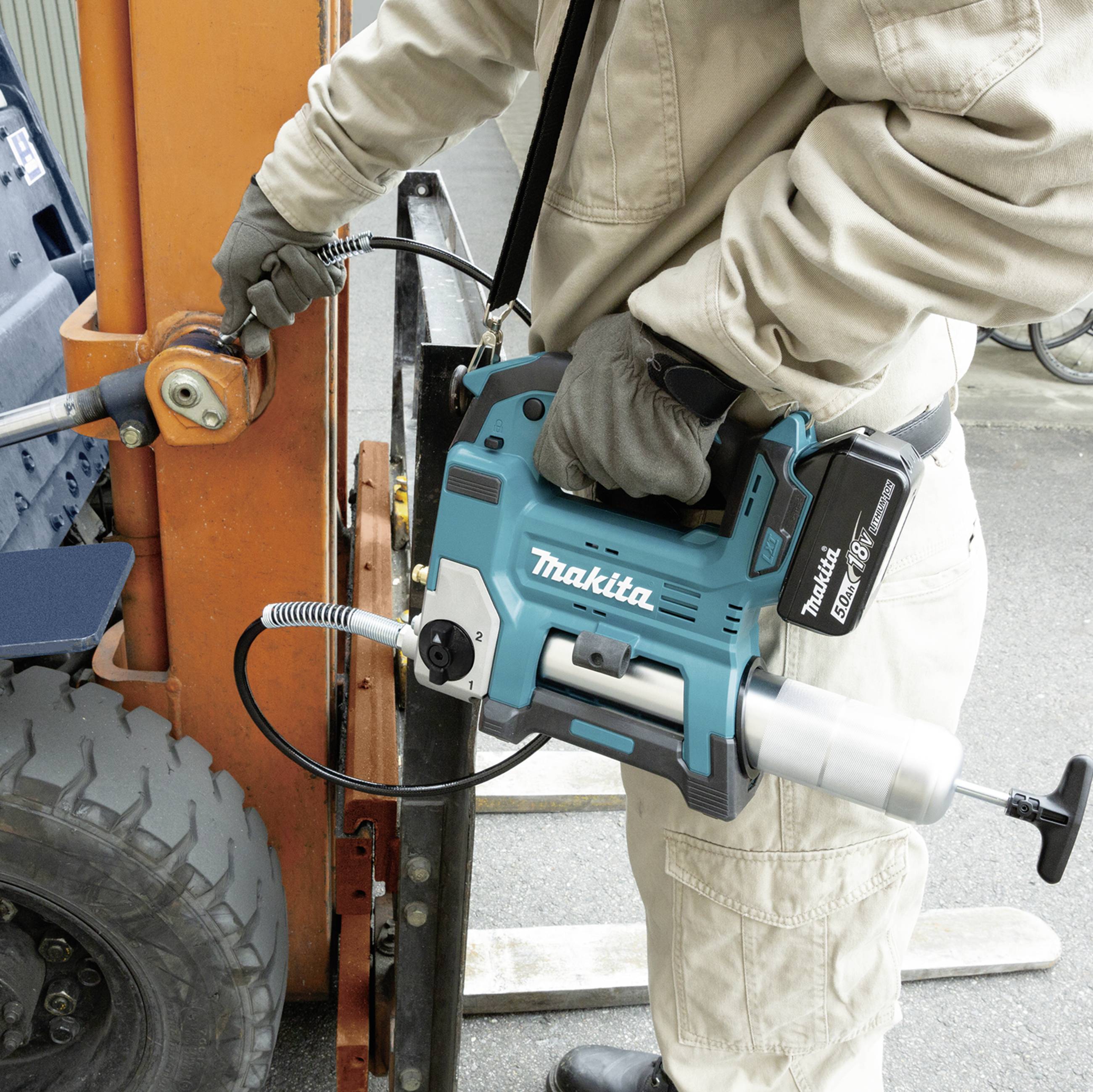 A person is using a Makita cordless drill to loosen a heavy machine connection. The scene depicts an industrial environment.
