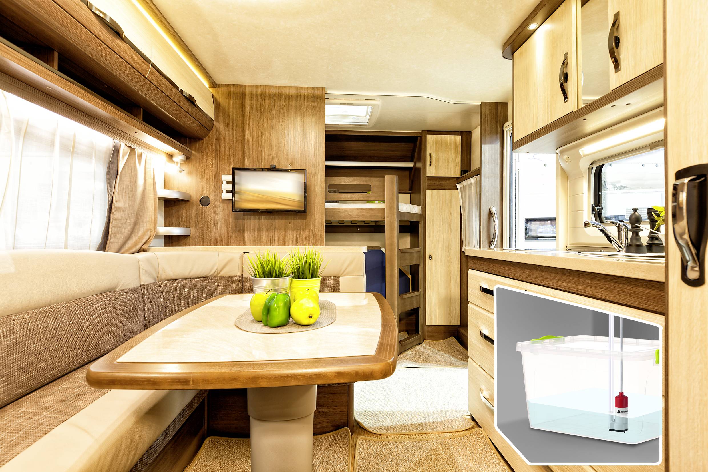 Interior of a motorhome with dining area, curtains, television and kitchen. Green apples are standing on the table in the foreground. Bottom left, a diagram shows a water system.