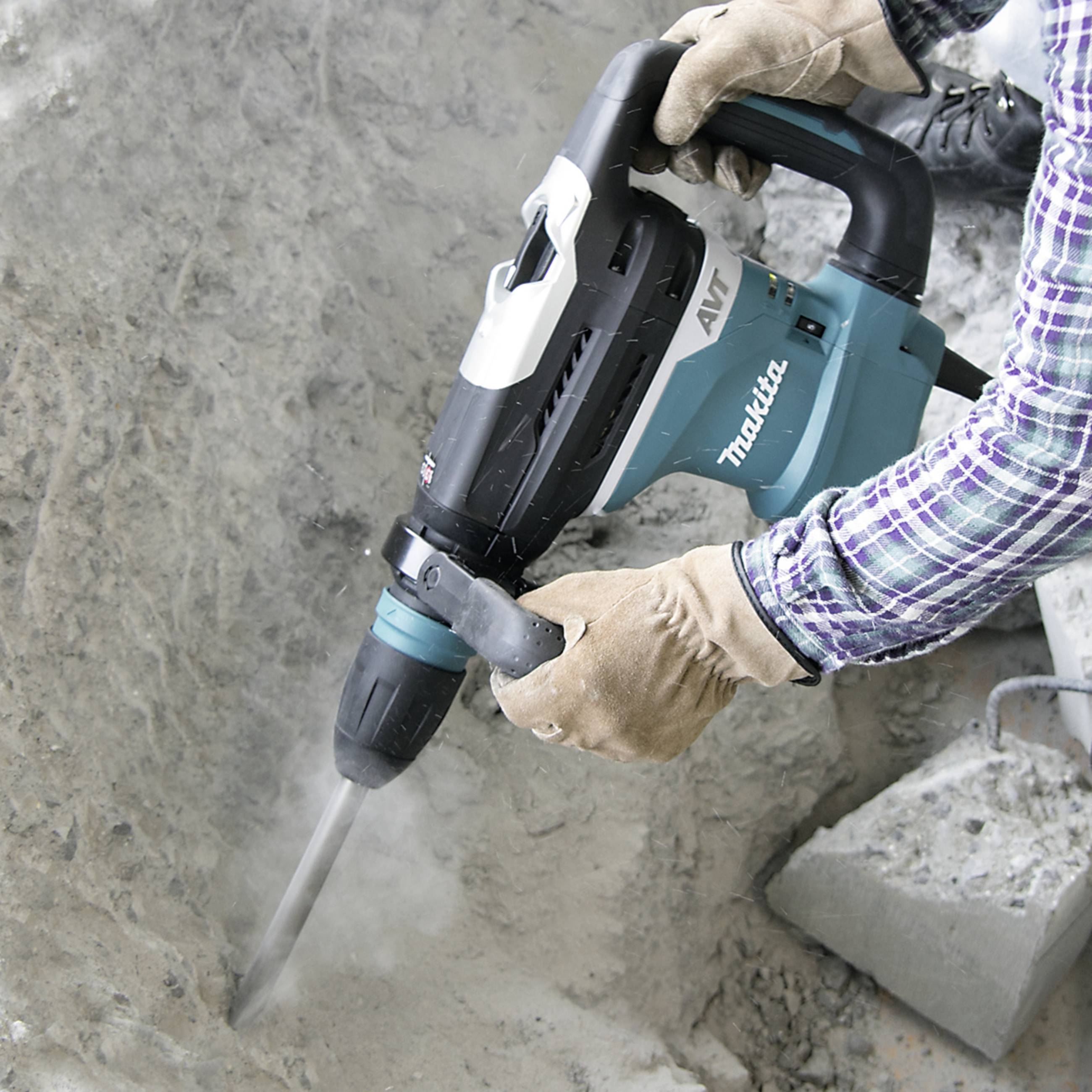 A person is using a hammer drill to work with concrete. Safety clothing is being worn. The tool is blue-white-grey.