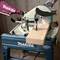 A Makita mitre saw precisely cuts a wooden board. An operator holds the tool handle for stability and control.