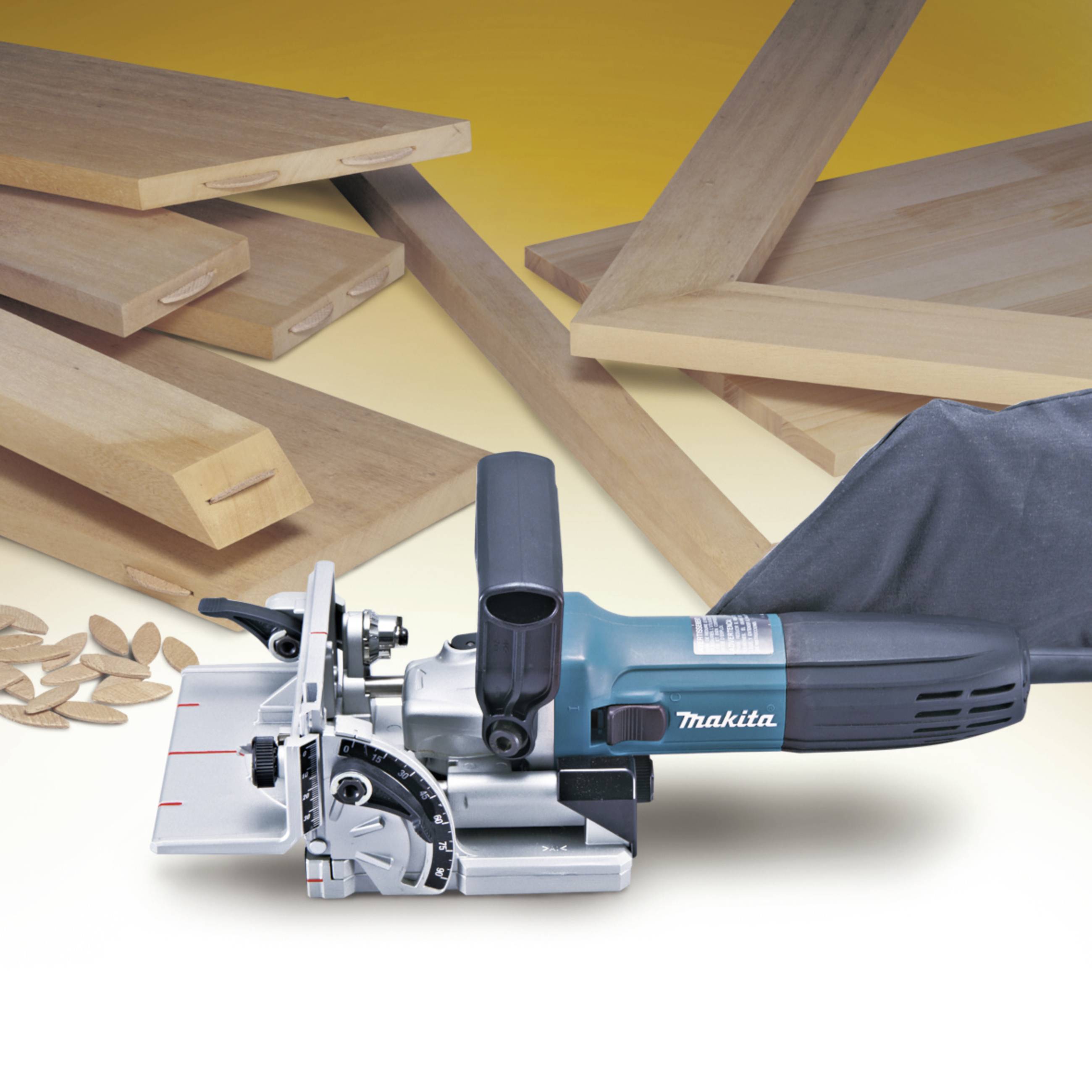 An electric wood router positioned in front of several wooden boards and connecting pieces, used for creating groove and tongue joints.