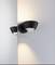 A modern wall light with a black casing casts warm light onto a light grey wall.