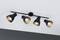 Four black ceiling spotlights, each with a single bulb, are mounted on a rail and fixed to a white ceiling.