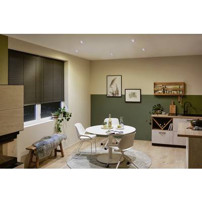 Cosy kitchen with a round white dining set, surrounded by plants, wooden shelves and a rug; warmly lit.
