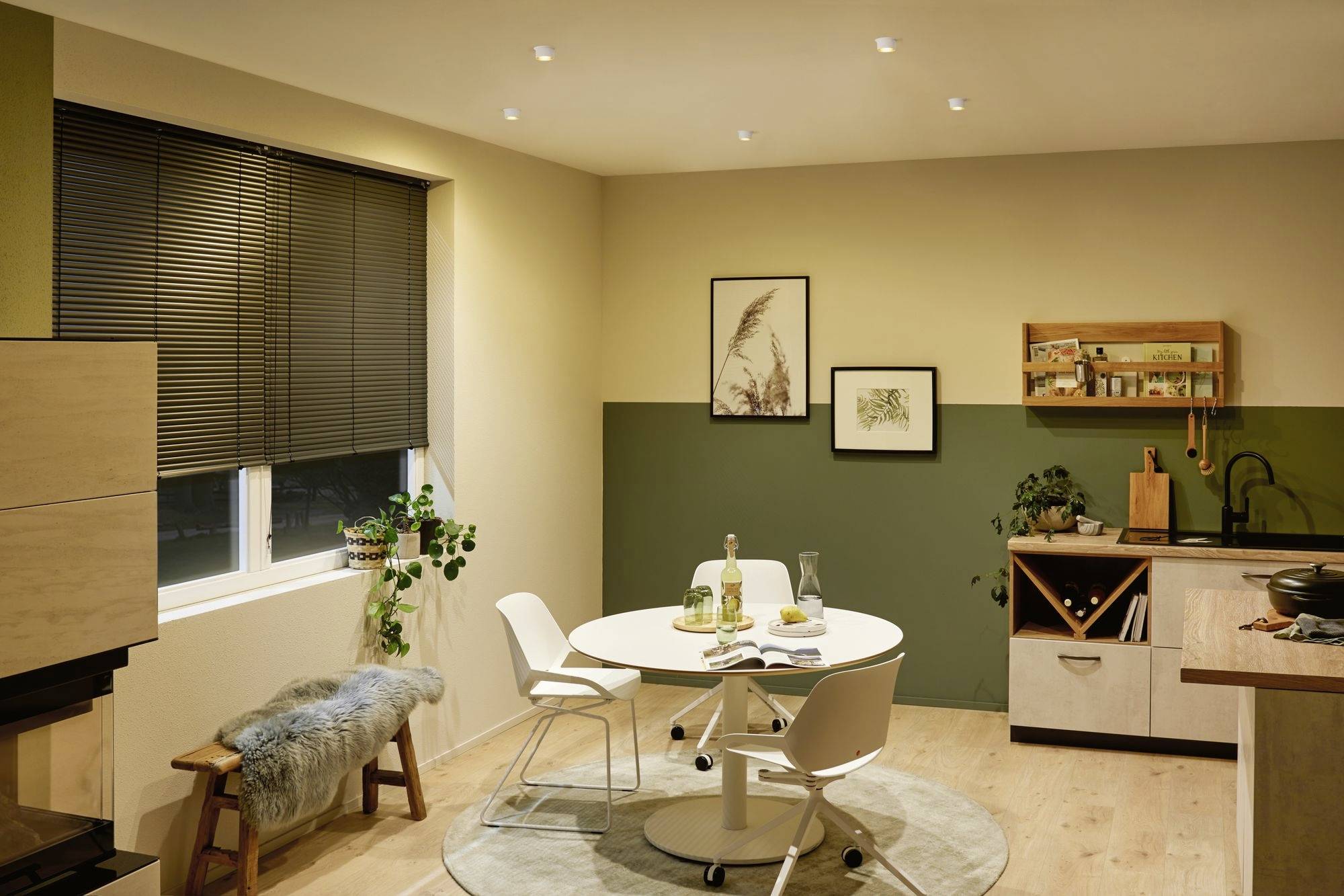 A stylishly decorated dining room with a round table and four chairs. Pictures hang on the wall, and plants are positioned on the windowsill and floor.