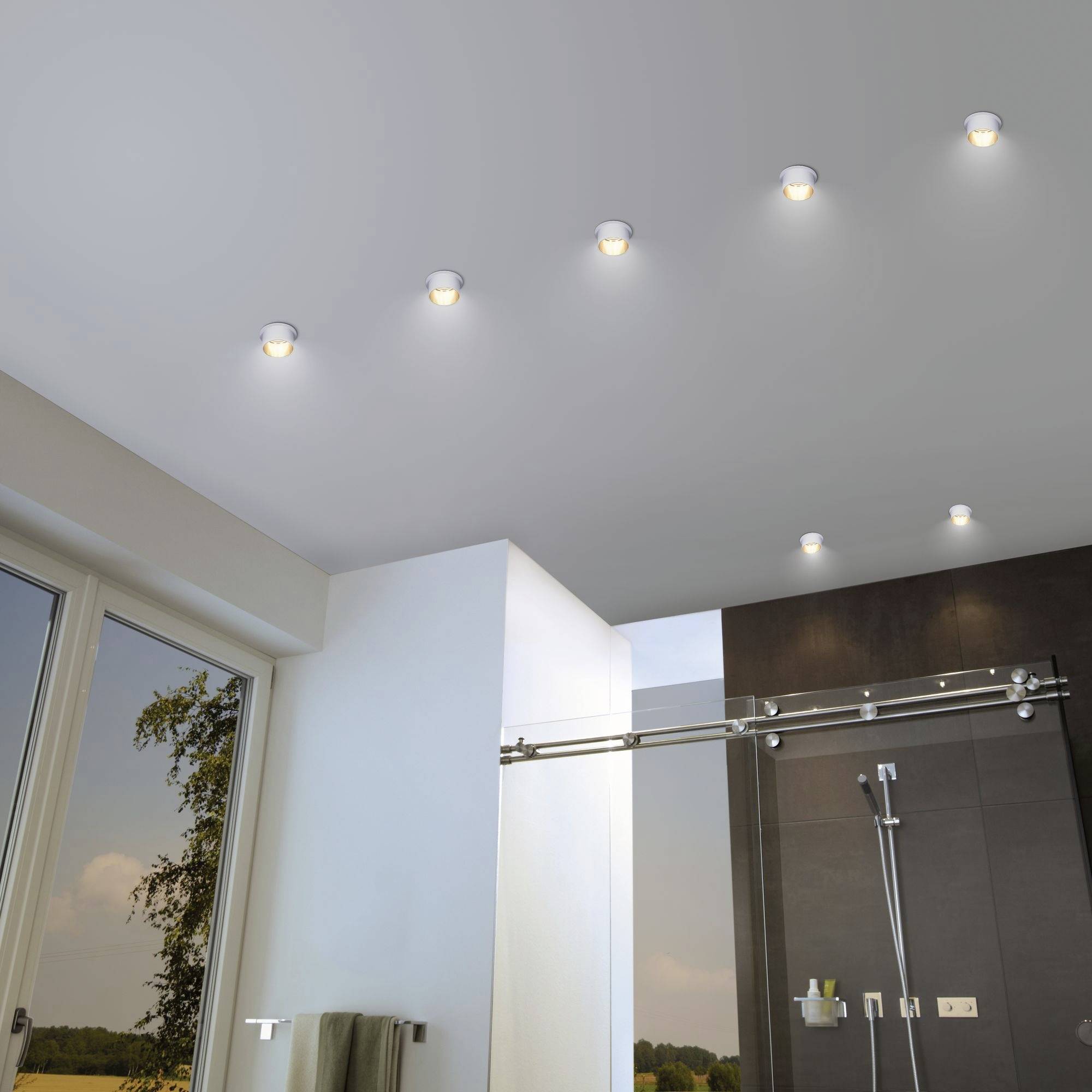 Modern bathroom ceiling with multiple recessed round lights, beneath which is a shower and a window with an outdoor view.
