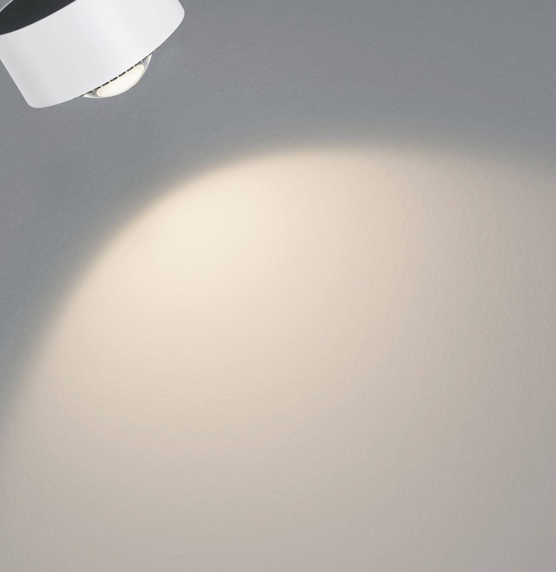 A ray of light from a ceiling light illuminates a grey wall.