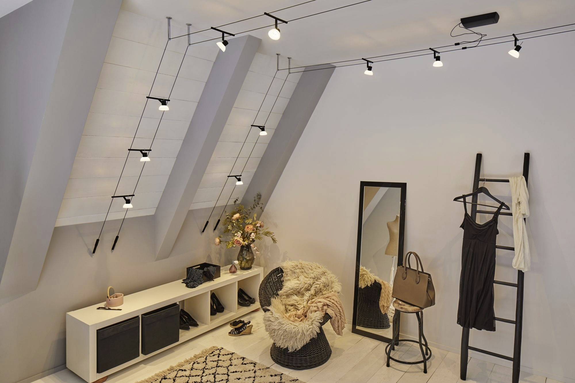 A stylishly furnished dressing room with a mirror, a chair, a decorative vase on the wardrobe, and a black dress draped over a ladder.