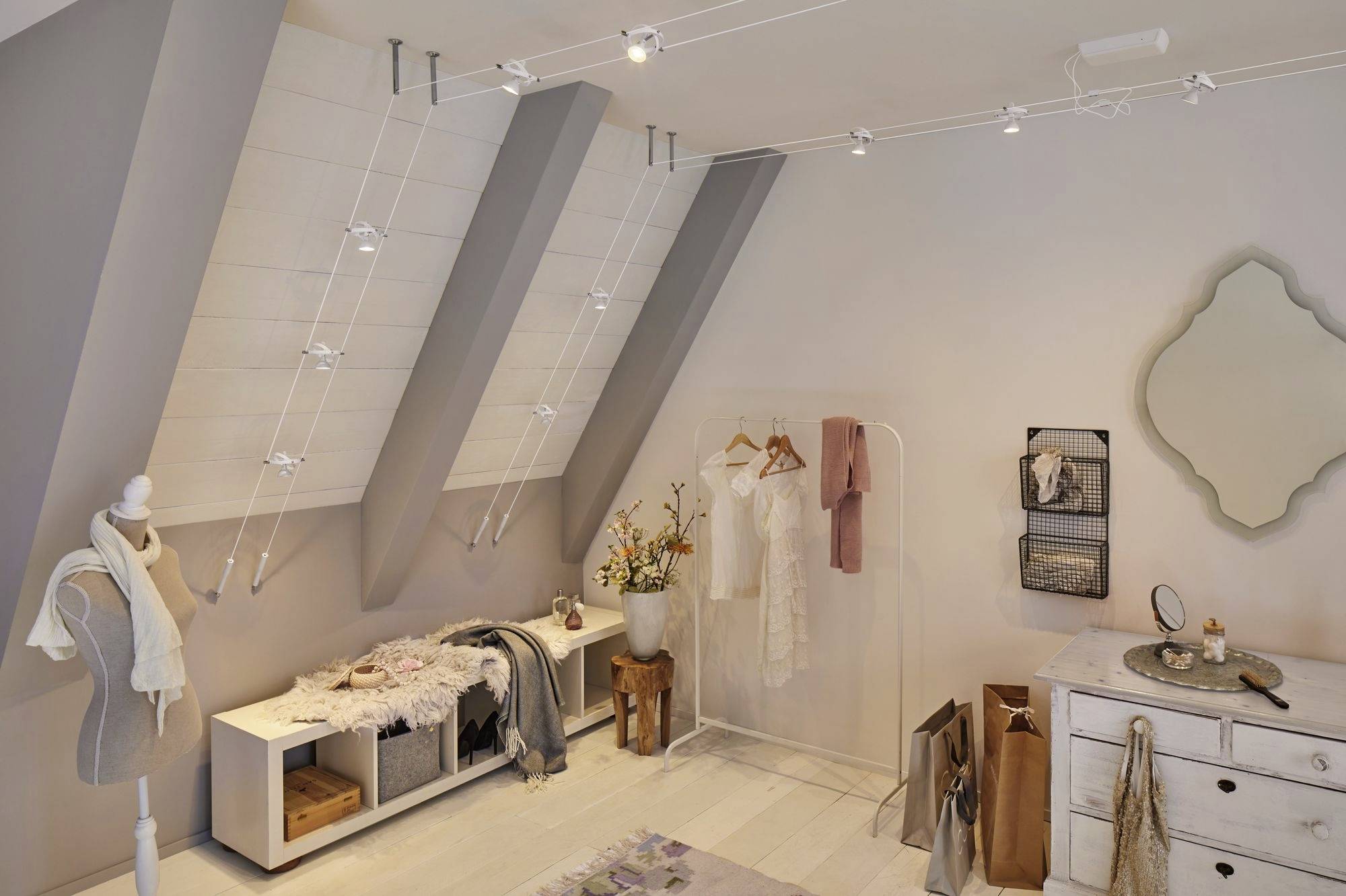 Loft bedroom with sloping walls, a decorative mirror, chest of drawers, coat hangers and a cosy, modern design.