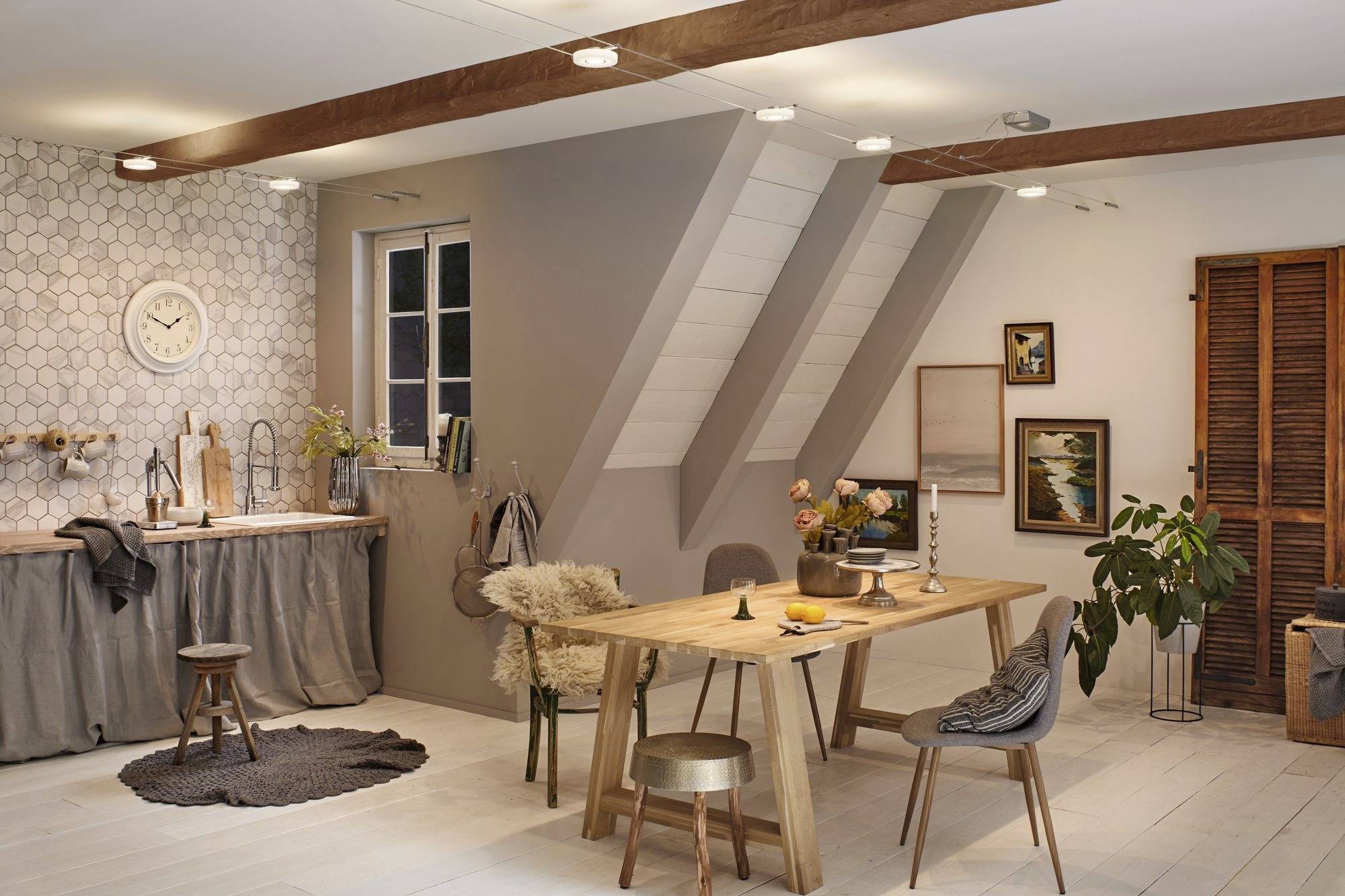 A modern dining room with a wooden table and chairs, decorated with plants and artwork. A window allows daylight to flood in.