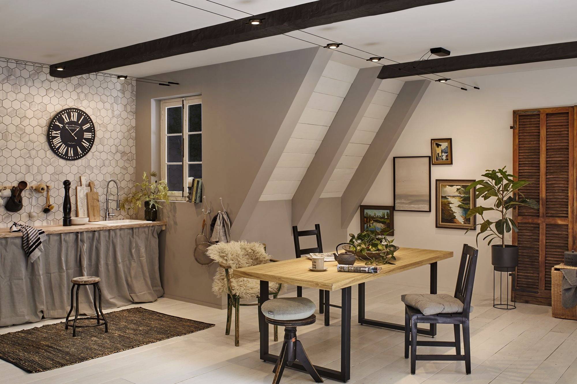 A cosy dining room with a wooden table and chairs. Decorative shelves and plants add warmth; a large clock hangs on the wall.