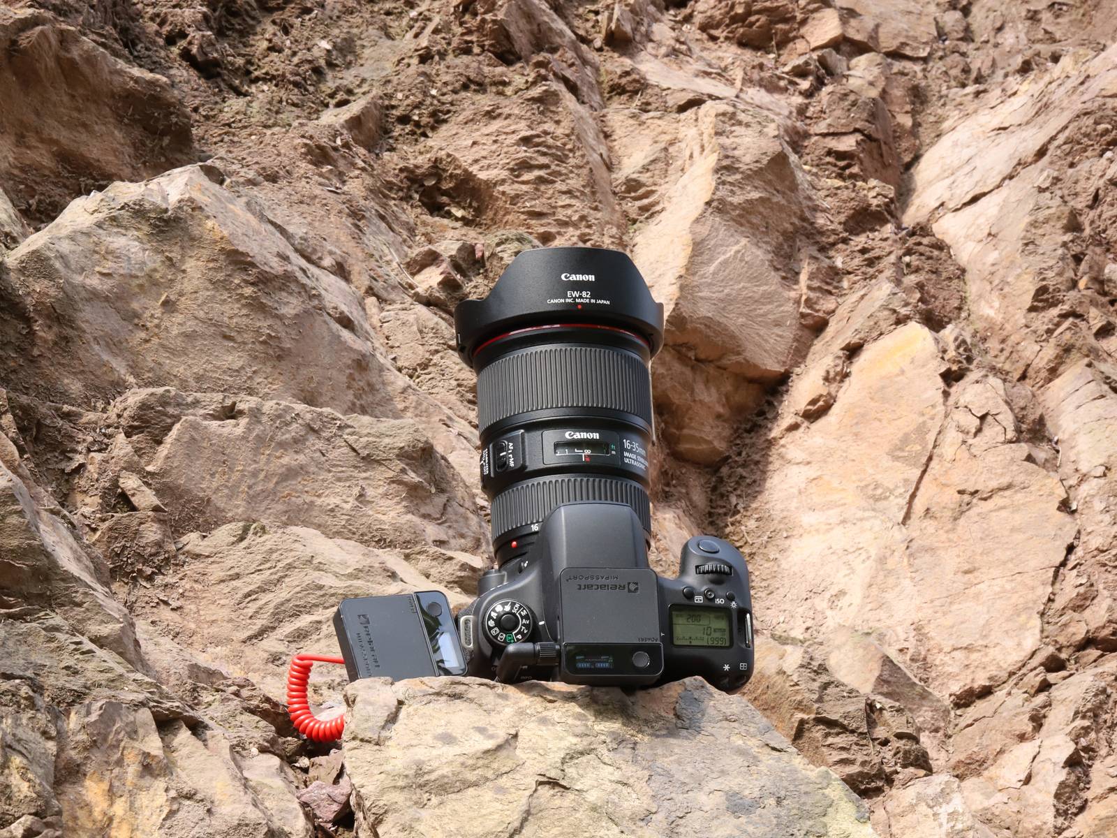 A professional camera rests on rocky ground, surrounded by brown stones.