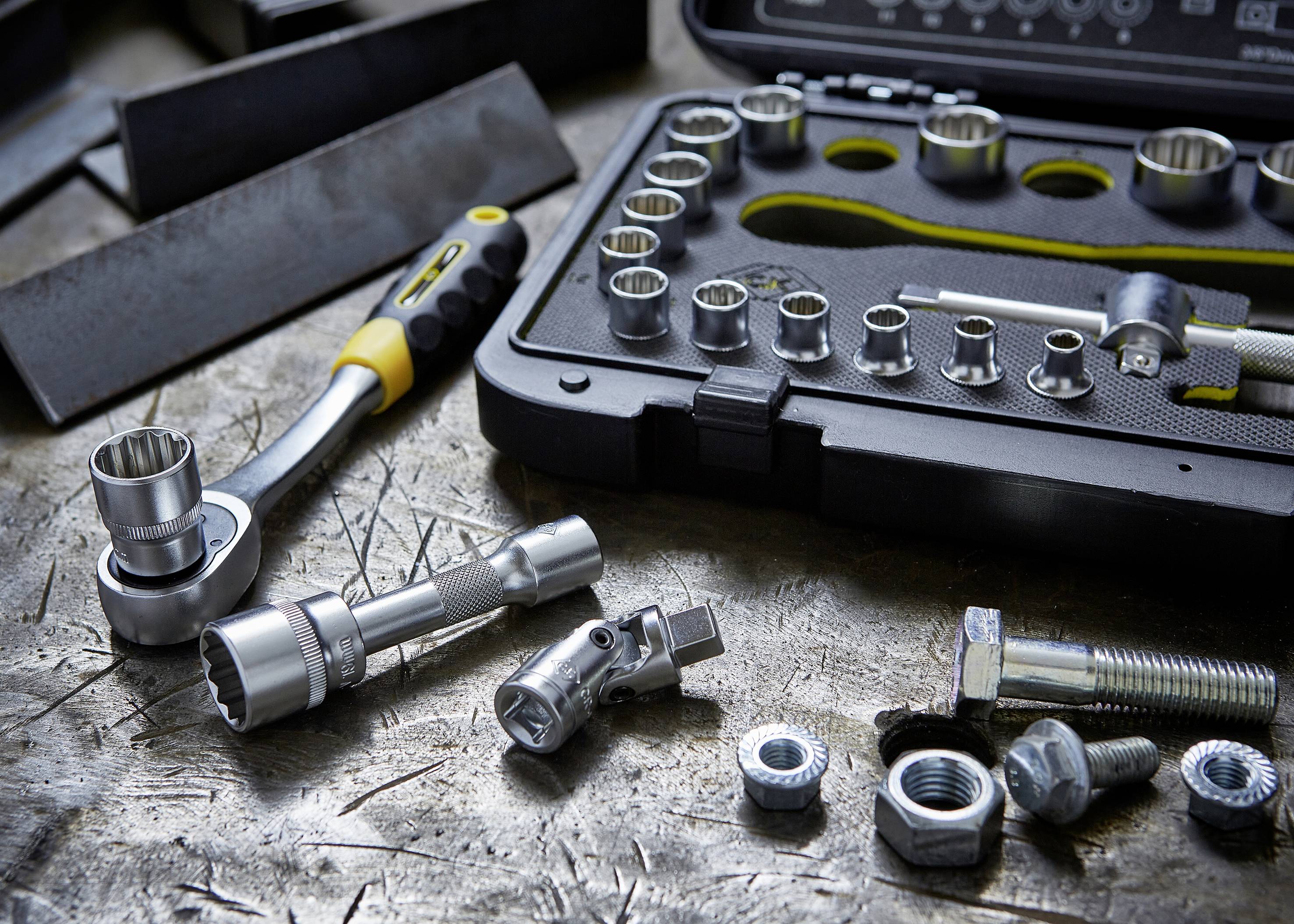 A ratchet set lies on a workshop table. It contains socket wrenches and extensions, alongside screws and nuts.