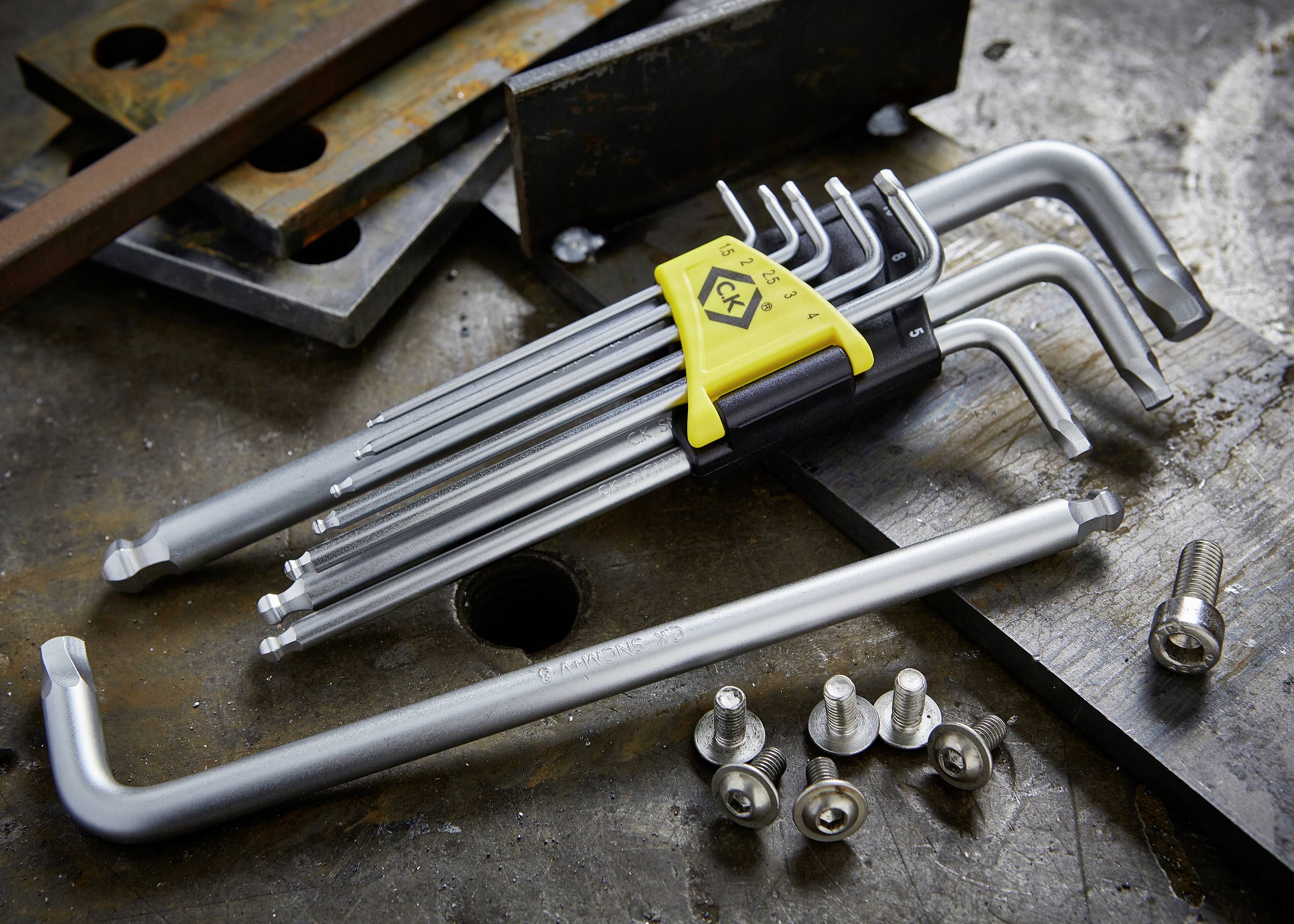 A set of Allen keys in various sizes lies on a workbench, surrounded by screws and metal plates.