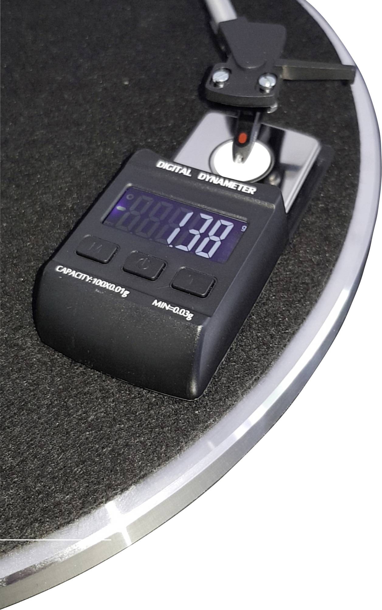 A digital dynamometer displays '1.37' when placed on a circular platform. The device measures weight or force.