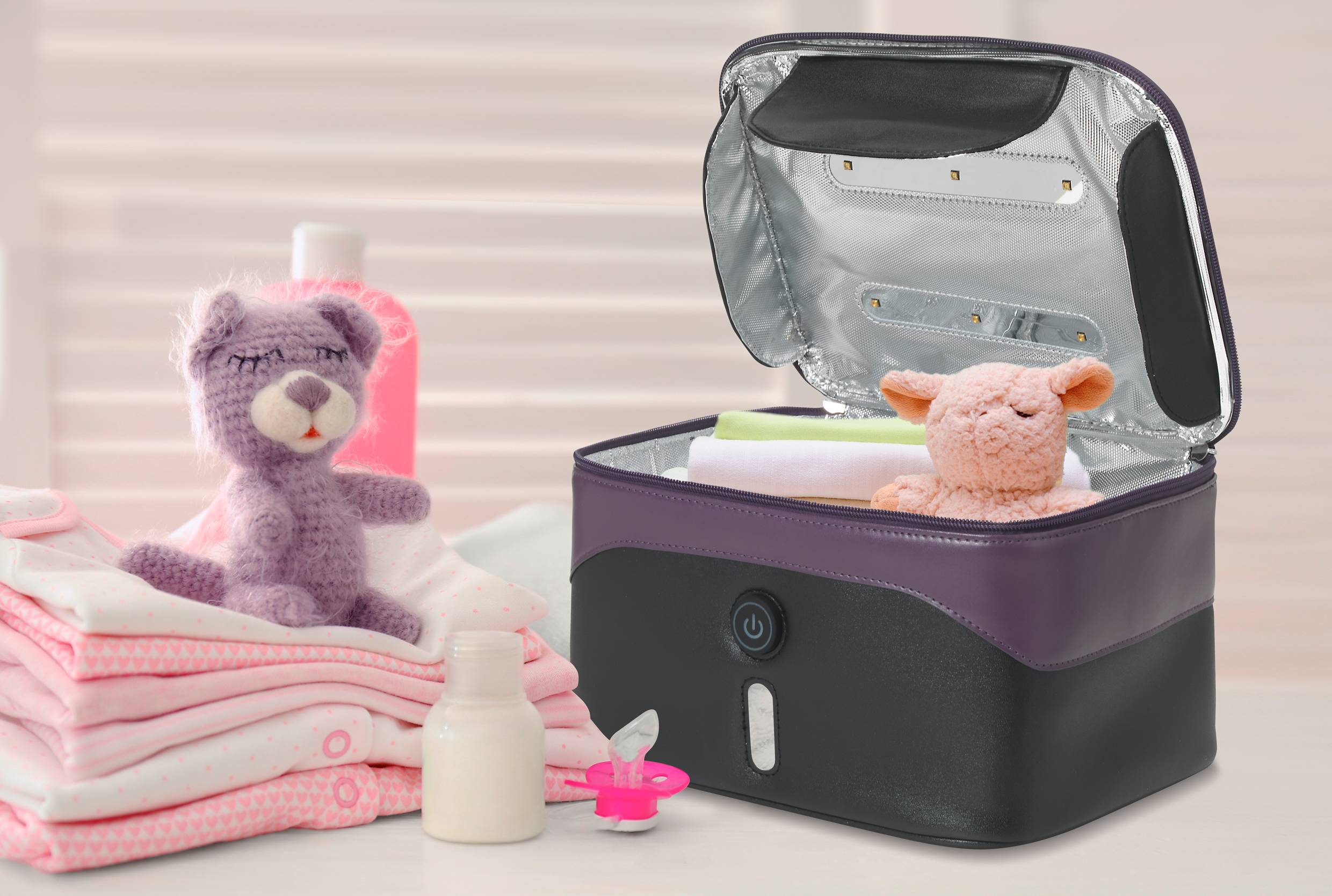An open, purple steriliser with a toy rabbit and baby bottles. Beside it, folded baby clothes and a soft toy.